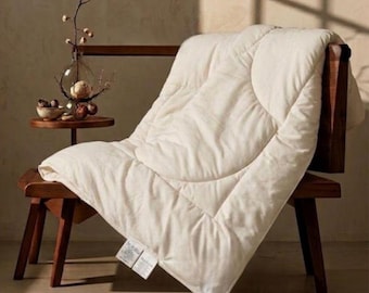 May include: A cream-colored quilted comforter with a circular stitched pattern draped over a dark wooden chair. The comforter features two white rectangular fabric labels attached to the bottom corner, displaying visible printed text.