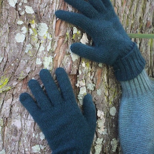 May include: A pair of dark green knitted gloves with a ribbed cuff. The gloves are shown against a textured bark background.