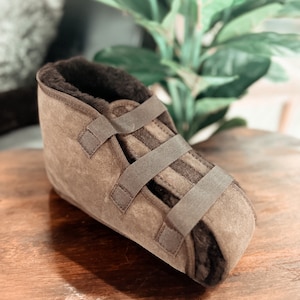 May include: A brown suede boot with a soft, brown fleece lining and adjustable straps. The boot is designed to provide support and comfort for the foot and ankle.
