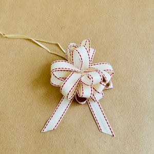 May include: A white ribbon bow with red stitching, tied with a loop for hanging.