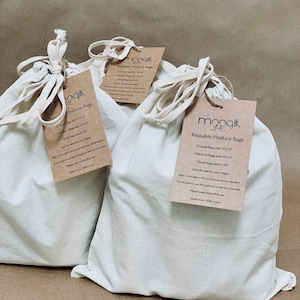 May include: Set of three reusable produce bags made from 100% cotton. The bags are white and come in three sizes: large, medium, and small. The bags have a drawstring closure and are labeled with the brand name "moogik".