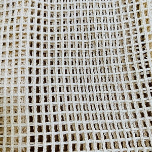May include: A close-up of a white crocheted mesh fabric. The fabric has a square grid pattern.