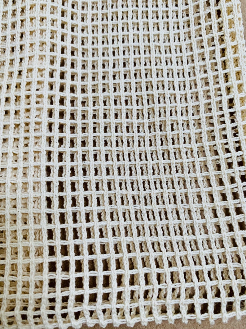 May include: A close-up of a white crocheted mesh fabric. The fabric has a square grid pattern.