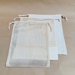 May include: Three reusable produce bags made of white mesh fabric with drawstring closures. The bags are stacked on top of each other on a brown background.
