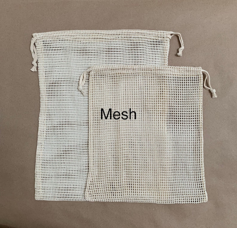 May include: Two white mesh produce bags with drawstring closures. The larger bag is behind the smaller bag. The smaller bag has the word "Mesh" printed on it.