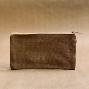 May include: A rectangular, olive-green canvas pouch with a beige zipper closure. The pouch is a simple, minimalist design, suitable for storing small items. The zipper pull is a matching beige color.