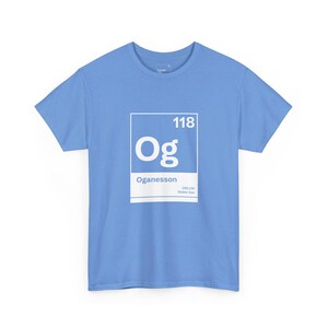 May include: A light blue t-shirt featuring a white square with the number "118" at the top and the letters "Og" in the center. Below the letters is the word "Oganesson". The shirt is a crew neck.