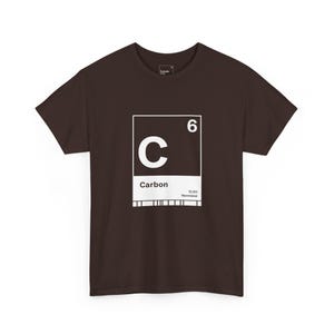 May include: A brown t-shirt with a white graphic of the element Carbon from the periodic table. The graphic shows the letter "C", the atomic number "6", the word "Carbon", and the atomic mass. The shirt is made of a soft material.