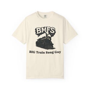 May include: Cream-colored t-shirt featuring a black and white illustration of a vintage steam train. Above the train is the text "BMFS" in a stylized font, and below the train, the text reads "BIG Train Song Guy."