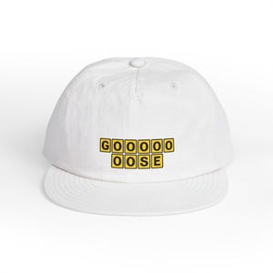 Könnte beinhalten: Weiße Baseballkappe mit dem Wort "GOOOOOOSE" in gelben und schwarzen Buchstabenkacheln. Die Kappe hat einen gebogenen Schirm und einen Knopf oben.