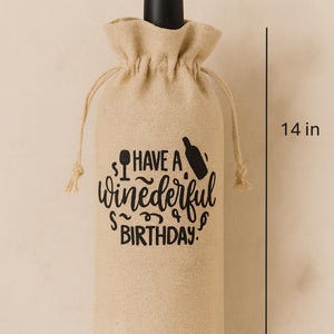 May include: A tan burlap wine bottle gift bag with a drawstring closure, featuring black printed text that reads "HAVE A winederful BIRTHDAY." with icons of a wine glass and bottle. The bag measures 14 inches in height and 6 inches in width.