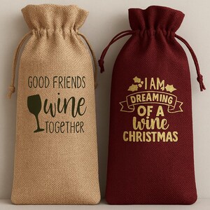 May include: Two drawstring wine bags with textured fabric. The left bag is tan with black text reading GOOD FRIENDS WINE TOGETHER and a wine glass icon. The right bag is deep red with gold text reading I AM DREAMING OF A WINE CHRISTMAS.