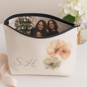 May include: A cream-colored zippered pouch featuring a watercolor floral design in peach and sage green, the initials S.H. in grey, and an interior photo print with the text My favorite people call me Grandma, finished with a gold tassel zipper pull.