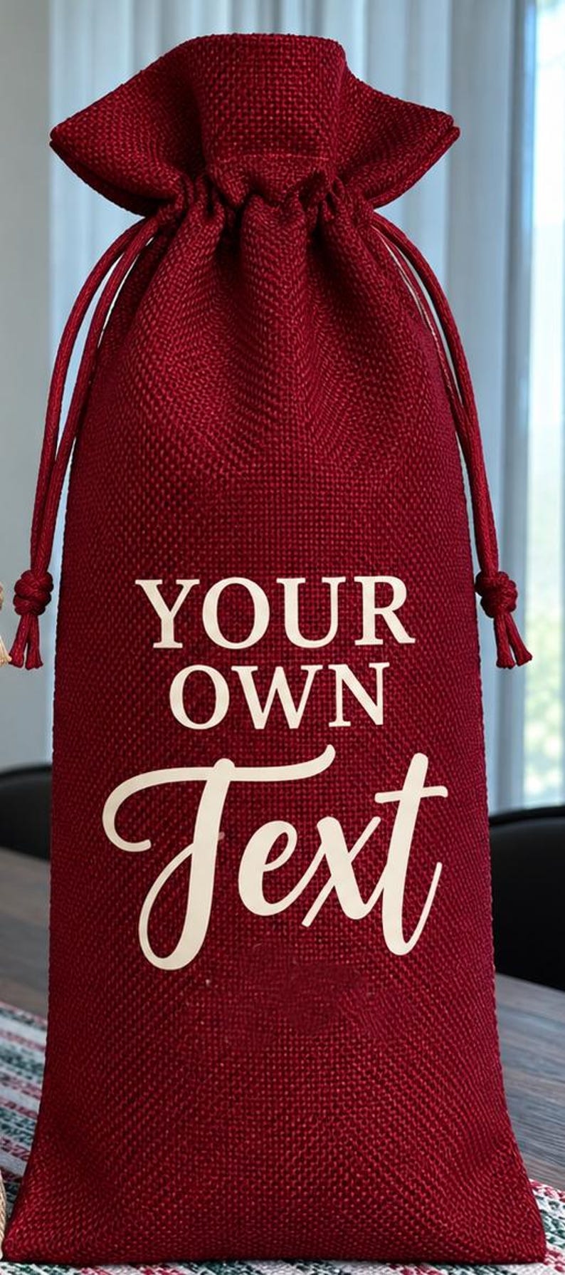 May include: A deep red burlap drawstring wine bottle bag featuring the white text YOUR OWN Text printed on the front. The bag has a textured woven fabric finish and matching red cord drawstrings that cinch at the top to secure the contents.