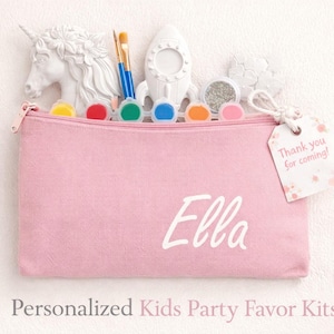 May include: A pink zippered pouch with the name "Ella" in white, containing art supplies and a unicorn figurine. The pouch is part of a personalized kids' party favor kit, with a tag that says "Thank you for coming!"