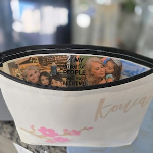 May include: A white canvas cosmetic bag with a black zipper, featuring a floral design and the word "Kowa" in a light brown script. Inside, a collage of family photos is visible, with the text "MY FAVORITE PEOPLE call me GRANDMA."