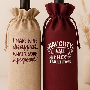 May include: Two wine bottle gift bags with drawstring closures. The left bag is tan with the text I MAKE WINE disappear. WHAT'S YOUR superpower? in dark red. The right bag is burgundy with the text NAUGHTY BUT nice I MULTITASK in white.