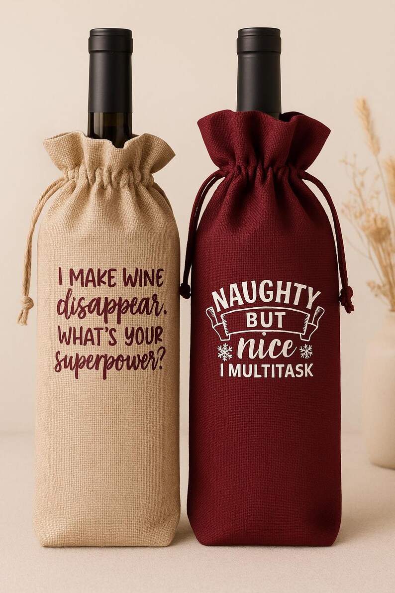 May include: Two wine bottle gift bags with drawstring closures. The left bag is tan with the text I MAKE WINE disappear. WHAT'S YOUR superpower? in dark red. The right bag is burgundy with the text NAUGHTY BUT nice I MULTITASK in white.