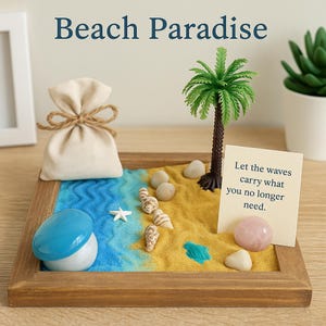 May include: A miniature beach scene in a wooden frame. It features a blue and yellow sand landscape with a palm tree, seashells, and a small bag. The text "Beach Paradise" is at the top, and a card reads "Let the waves carry what you no longer need."