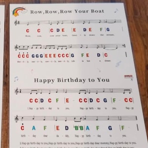 May include: Sheet music with the lyrics and notes for "Row, Row, Row Your Boat" and "Happy Birthday to You." The text is in black, with some notes in red and blue. A rainbow graphic is at the top.