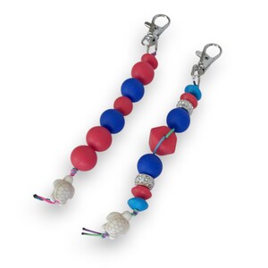 May include: Two beaded keychains with lobster claw clasps. One keychain features red and blue round beads, while the other has a mix of round, square, and rhinestone beads in red, blue, and turquoise. Both have turtle charms.