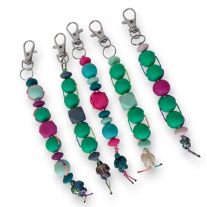 May include: Five beaded keychains with silver-tone clasps. Each keychain features a unique combination of colorful beads in shades of green, pink, blue, and gray. Some keychains have small turtle charms.