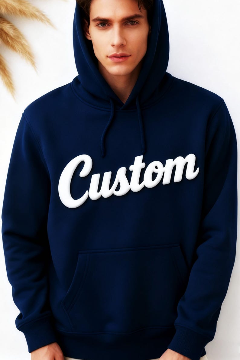 May include: Navy blue hoodie with the word "Custom" in white, stylized lettering across the chest. The hoodie features a hood with drawstrings and a front pocket. The garment is made of a soft material.