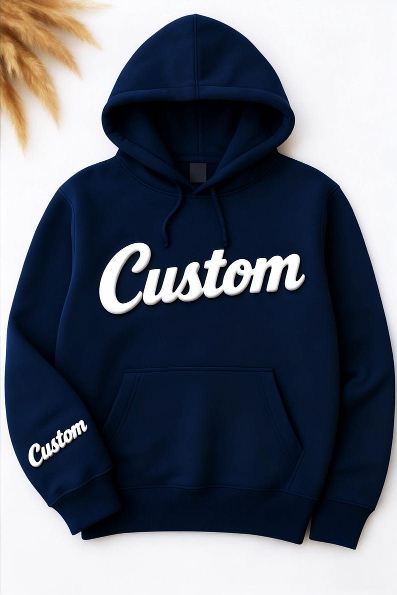 May include: Navy blue hoodie with the word "Custom" in white, bold, cursive lettering across the chest. The same word is also printed on the left sleeve. The hoodie has a hood and a front pocket.