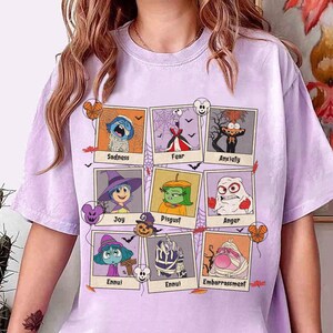 May include: A light purple t-shirt featuring nine framed cartoon illustrations of emotions, including Sadness, Fear, and Joy. Each frame has a Halloween theme with bats, spiders, and pumpkins. The shirt is a comfortable, oversized fit.