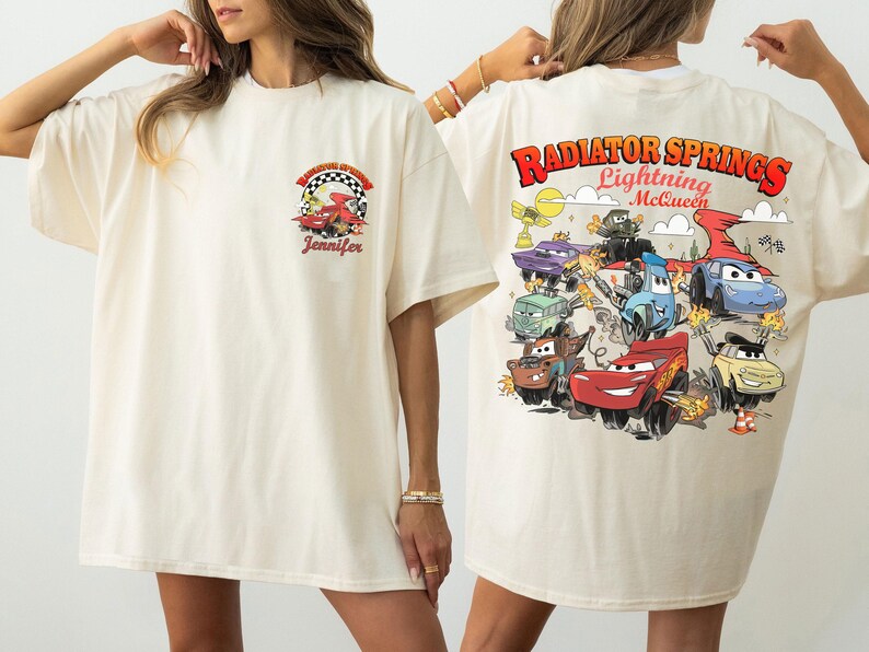 Pode incluir: Camiseta creme com um gr&aacute;fico colorido do filme Carros. A frente tem um pequeno design com um carro de corrida e o nome "Jennifer". A parte de tr&aacute;s exibe "Radiator Springs Lightning McQueen" com v&aacute;rios personagens de carros.