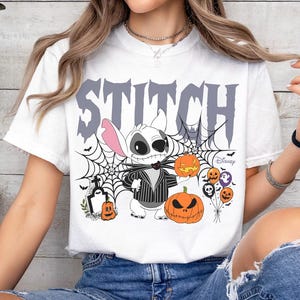 Pode incluir: Camiseta branca com um design de Halloween com a palavra "STITCH" em letras cinzentas. O design inclui Stitch vestido como Jack Skellington, ab&oacute;boras, teias de aranha e a marca Disney.