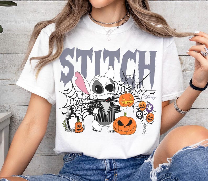 Pode incluir: Camiseta branca com um design de Halloween com a palavra "STITCH" em letras cinzentas. O design inclui Stitch vestido como Jack Skellington, ab&oacute;boras, teias de aranha e a marca Disney.