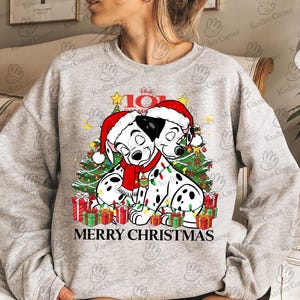 May include: A gray sweatshirt featuring a festive design with two Dalmatian dogs wearing Santa hats and a red scarf, surrounded by Christmas trees and wrapped gifts. The text "MERRY CHRISTMAS" is displayed below the dogs. A Disney 101 Dalmatians design.