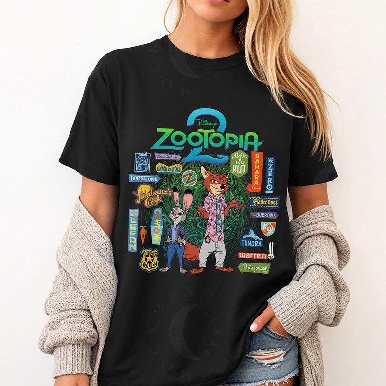 Op de afbeelding: Zwart T-shirt met een ontwerp uit de Disney-film "Zootopia". Het ontwerp bevat de titel van de film, personages en stadsborden. Het T-shirt heeft een ronde hals en korte mouwen.