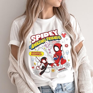 Puede incluir: Camiseta blanca con el texto "Spidey and His Amazing Friends" e ilustraciones de dibujos animados de Spider-Man, Spider-Gwen y Miles Morales. El dise&ntilde;o incluye elementos de c&oacute;mic como bocadillos y estrellas.