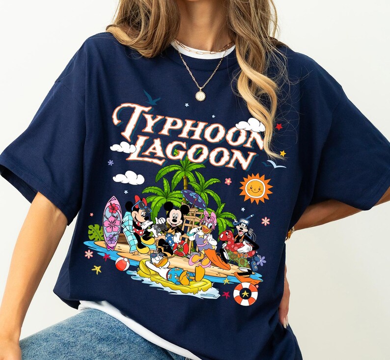 May include: Navy blue t-shirt featuring the words "Typhoon Lagoon" above a colorful graphic of Disney characters at a tropical beach. The graphic includes Mickey Mouse, Minnie Mouse, Donald Duck, and Goofy.
