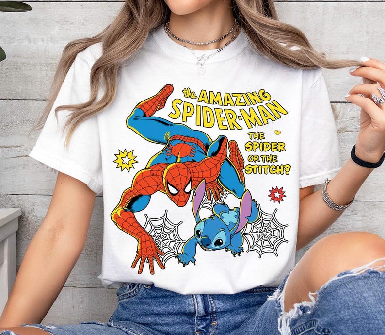 May include: White t-shirt featuring a colorful graphic of Spider-Man and Stitch. The design includes the text "THE AMAZING SPIDER-MAN" and "THE SPIDER OR THE STITCH?" The illustration is in a comic book style with vibrant colors and web details.