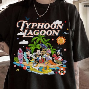 May include: Black t-shirt featuring a colorful graphic of Disney characters at Typhoon Lagoon. The design includes Mickey Mouse, Minnie Mouse, Donald Duck, and Goofy, along with palm trees, a sun, and the words "Typhoon Lagoon".