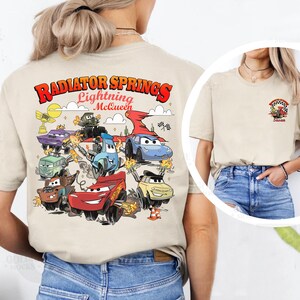 Pode incluir: Camiseta bege com um gr&aacute;fico colorido de personagens do filme Carros, incluindo Rel&acirc;mpago McQueen. O texto "Radiator Springs Lightning McQueen" &eacute; impresso na parte superior. Um gr&aacute;fico menor est&aacute; na frente.