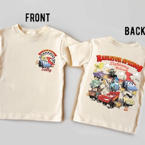 Pode incluir: Camiseta creme com um desenho de desenho animado do filme Carros. A frente mostra Sally e o texto "Sally". A parte de tr&aacute;s da camisa apresenta Rel&acirc;mpago McQueen e outros personagens com o texto "Radiator Springs Lightning McQueen".