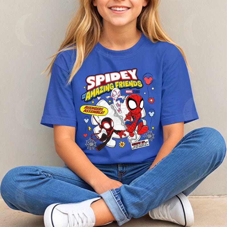 Puede incluir: Una camiseta azul con las palabras "Spidey and His Amazing Friends" y dibujos animados de Spider-Man, Spider-Gwen y Miles Morales. La camiseta tambi&eacute;n tiene las palabras "Avengers Assemble!" en un bocadillo amarillo.