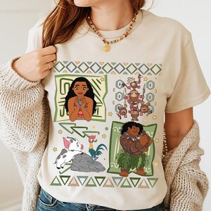 May include: Beige t-shirt featuring four square panels with cartoon characters. The panels include Moana, a group of Kakamora, Pua and Hei Hei, and Maui. The shirt has a geometric design in green and yellow.