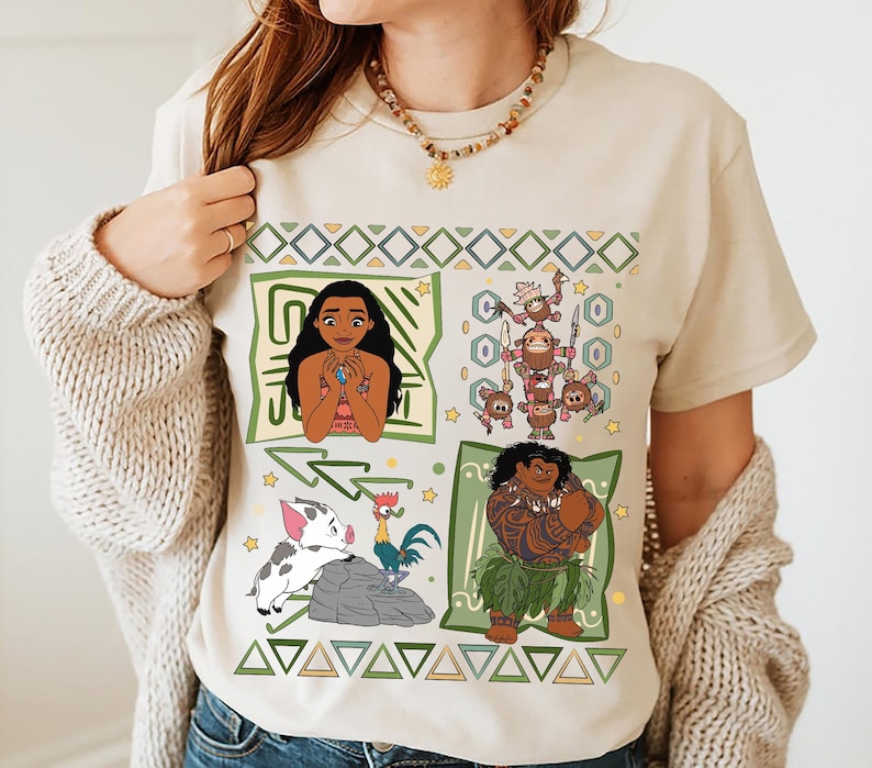 May include: Beige t-shirt featuring four square panels with cartoon characters. The panels include Moana, a group of Kakamora, Pua and Hei Hei, and Maui. The shirt has a geometric design in green and yellow.