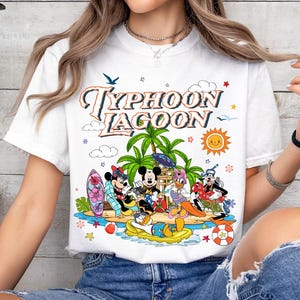 May include: White t-shirt featuring a colorful graphic of Disney characters at Typhoon Lagoon. The design includes Mickey and Minnie Mouse, Donald Duck, and Goofy, with palm trees, a sun, and the words "Typhoon Lagoon".