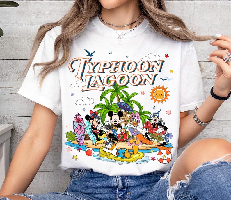 May include: White t-shirt featuring a colorful graphic of Disney characters at Typhoon Lagoon. The design includes Mickey and Minnie Mouse, Donald Duck, and Goofy, with palm trees, a sun, and the words "Typhoon Lagoon".