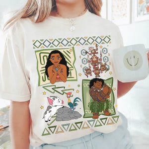 May include: Cream-colored t-shirt featuring cartoon illustrations of characters from the animated movie Moana. The design includes Moana, Maui, Pua, Hei Hei, and the Kakamora, surrounded by geometric patterns.