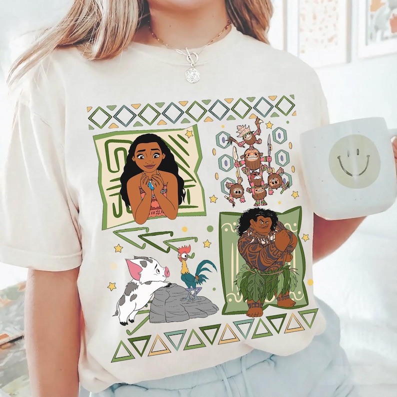 May include: Cream-colored t-shirt featuring cartoon illustrations of characters from the animated movie Moana. The design includes Moana, Maui, Pua, Hei Hei, and the Kakamora, surrounded by geometric patterns.