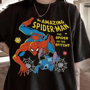 May include: Black t-shirt featuring a graphic of Spider-Man and Stitch. The design includes the text "the AMAZING SPIDER-MAN" in yellow, with the question "THE SPIDER OR THE STITCH?" The shirt has a crew neck and short sleeves.