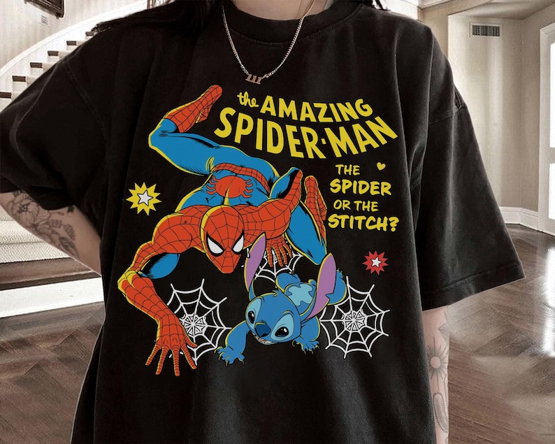 May include: Black t-shirt featuring a graphic of Spider-Man and Stitch. The design includes the text "the AMAZING SPIDER-MAN" in yellow, with the question "THE SPIDER OR THE STITCH?" The shirt has a crew neck and short sleeves.
