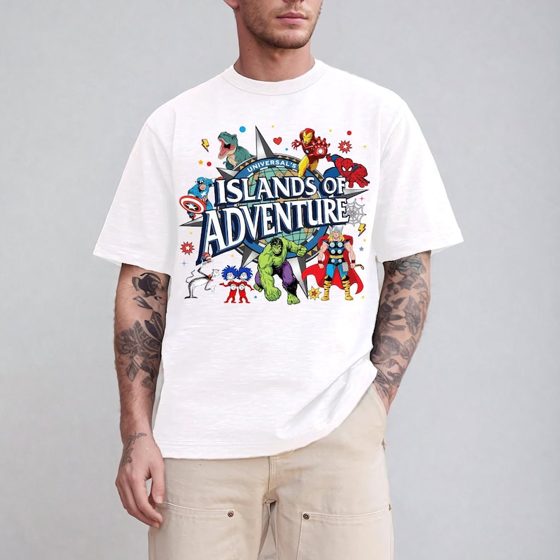 May include: White t-shirt featuring a colorful graphic of various Marvel characters and the text "UNIVERSAL ISLANDS OF ADVENTURE". The design includes Iron Man, Spider-Man, Hulk, and Thor. The shirt is a classic crew neck style.
